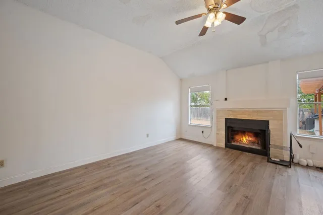 an empty room with wooden floor fireplace cabinet and windows