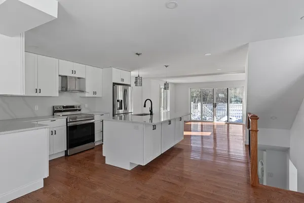 a large white kitchen with stainless steel appliances granite countertop a stove and white cabinets with wooden floor