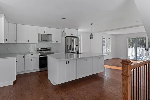 a kitchen with stainless steel appliances granite countertop a stove top oven a sink a refrigerator with white cabinets and wooden floor