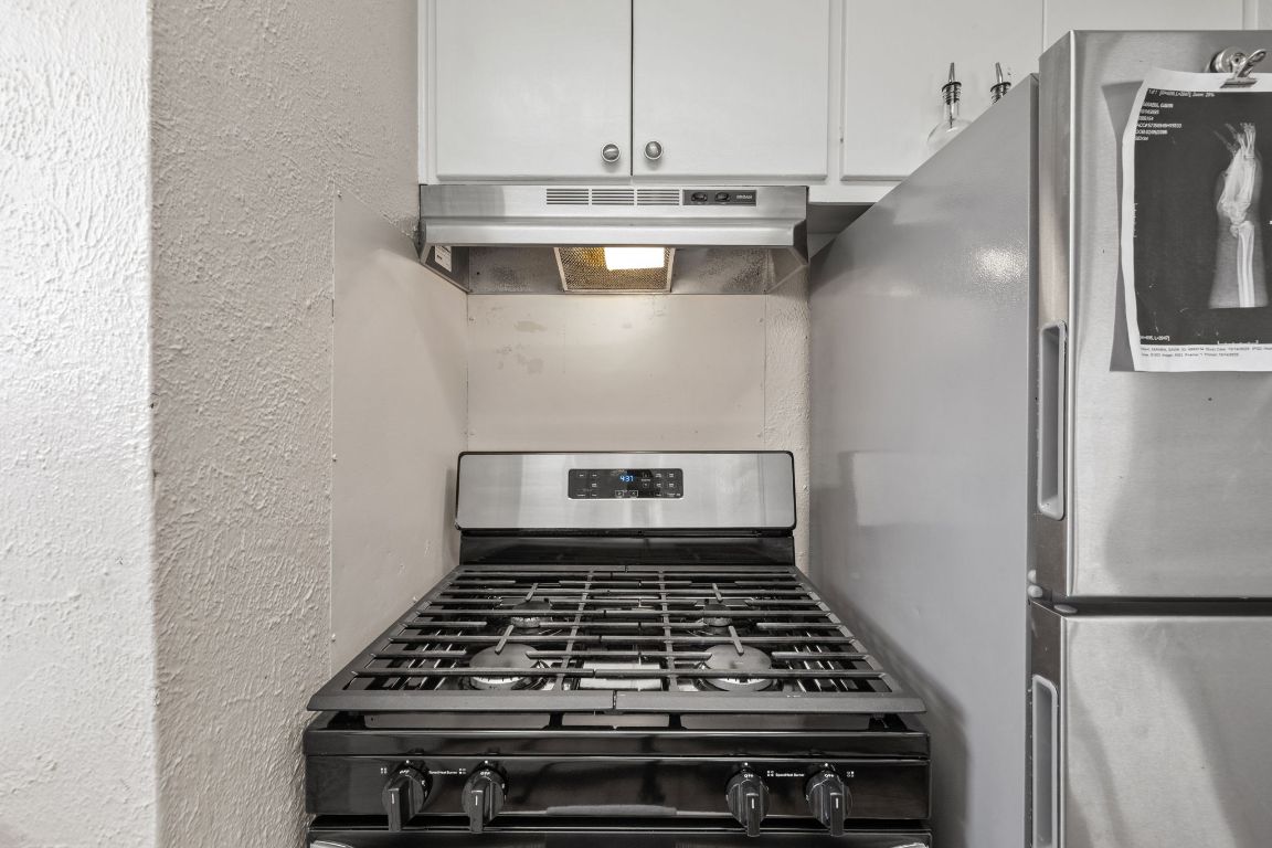 1202 East 29th Street, Unit A Austin, TX 78722 - Photo 14 of 37 Kitchen featuring range with gas stovetop, under cabinet range hood, a textured wall, and white cabinetry