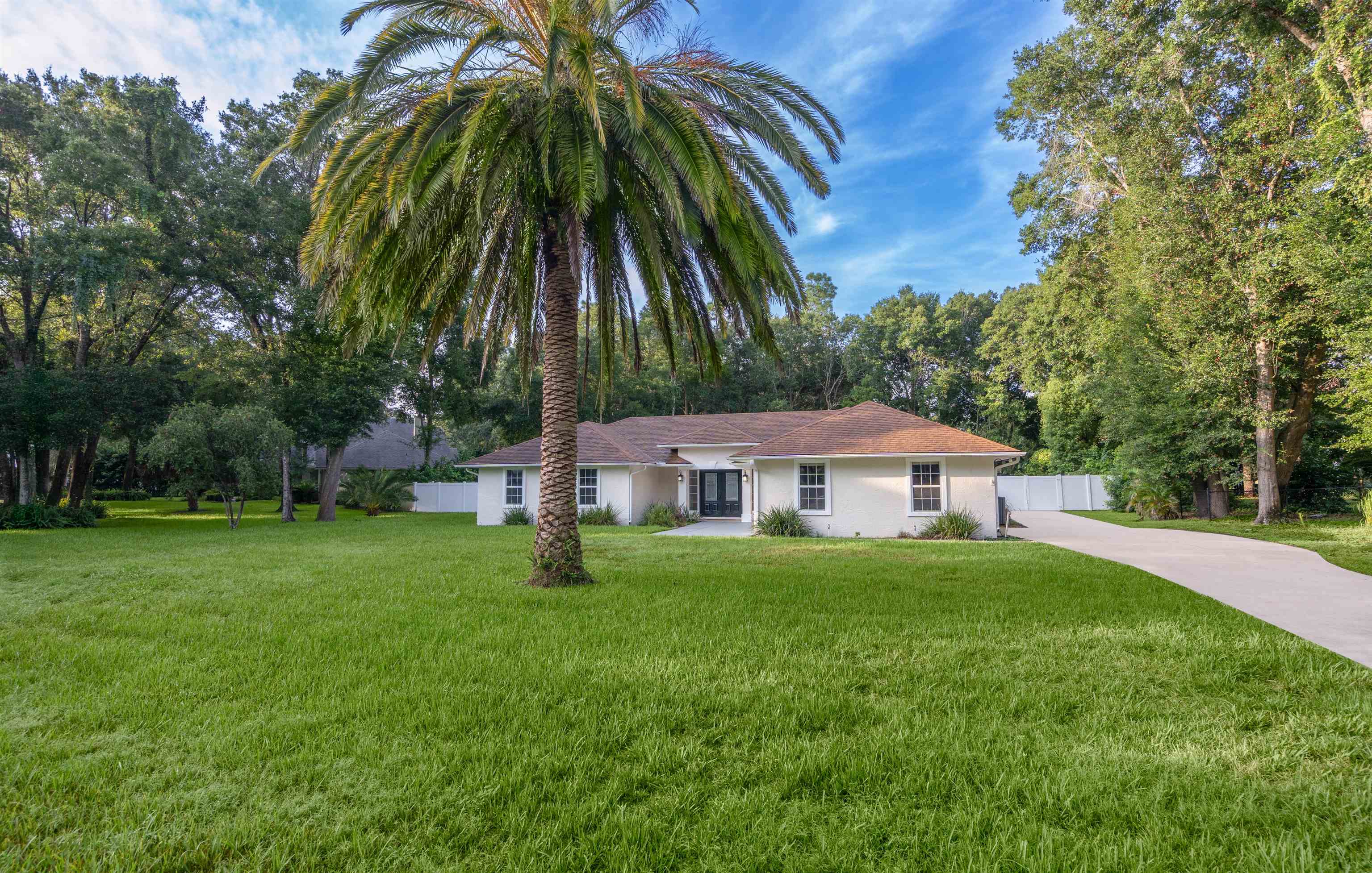 Ranch-style house with concrete driveway, stucco siding, and view of scattered trees