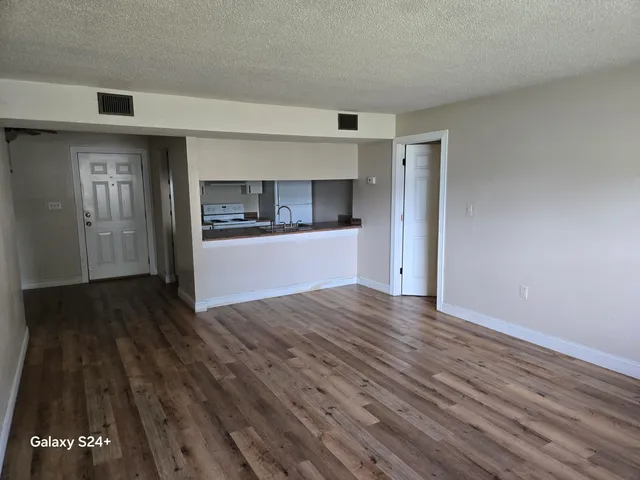 a view of empty room with wooden floor and kitchen