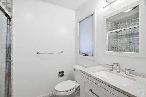 a bathroom with a granite countertop toilet a sink a mirror and a window
