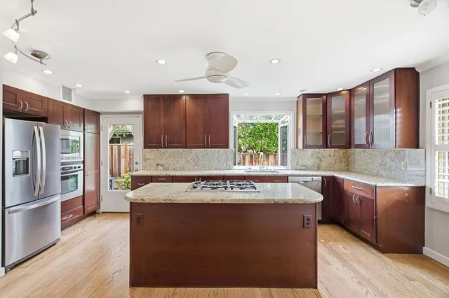 a kitchen with stainless steel appliances granite countertop a refrigerator a sink and a stove with wooden floor