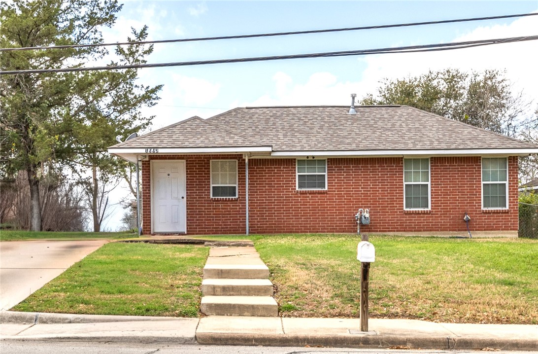 View of front of property featuring roof with shingles, a front lawn, and brick siding