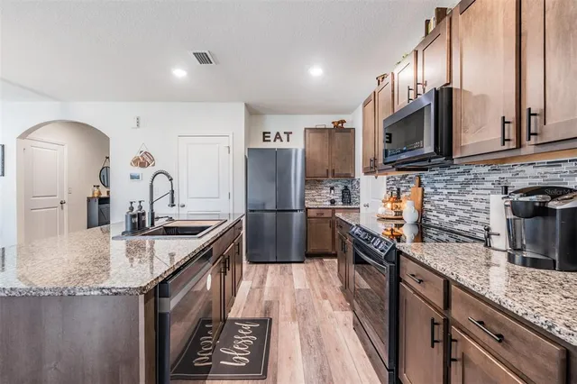 a kitchen with stainless steel appliances granite countertop a sink a stove and a wooden floors