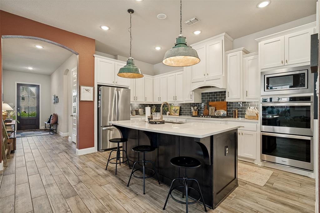 14948 Gentry Drive Aledo, TX 76008 - Photo 10 of 25 Kitchen featuring a large island with white countertop, white cabinetry, dark subway tile backsplash, stainless steel appliances, and wood-finish flooring