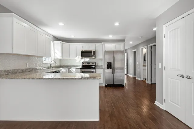 a kitchen with stainless steel appliances granite countertop a refrigerator a stove top oven a sink and dishwasher with wooden floor