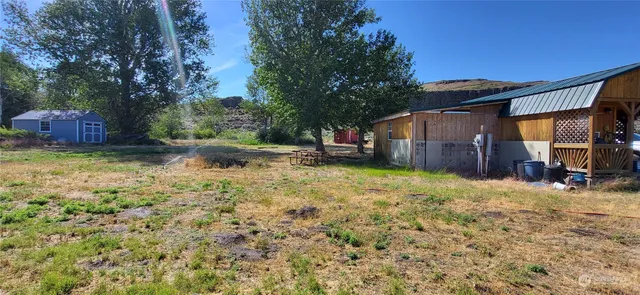 a view of a backyard with large trees and a small barn