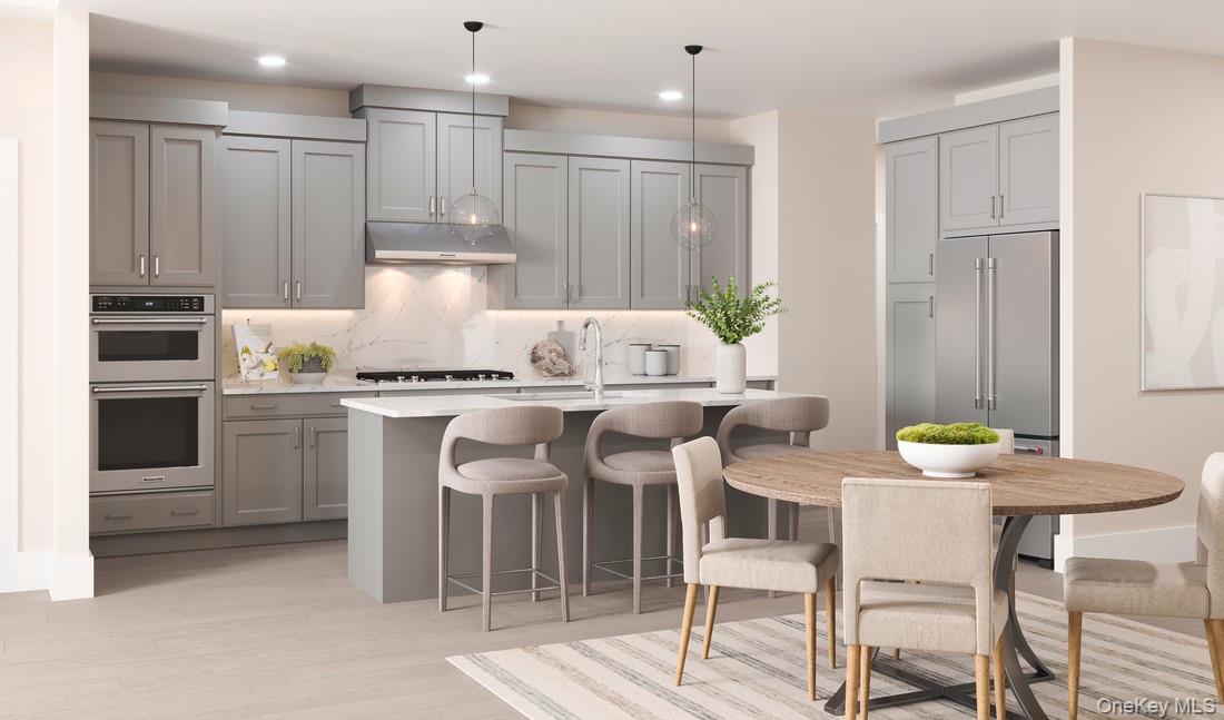 Kitchen featuring gray cabinets, stainless steel appliances, hanging light fixtures, backsplash, and a kitchen island with sink