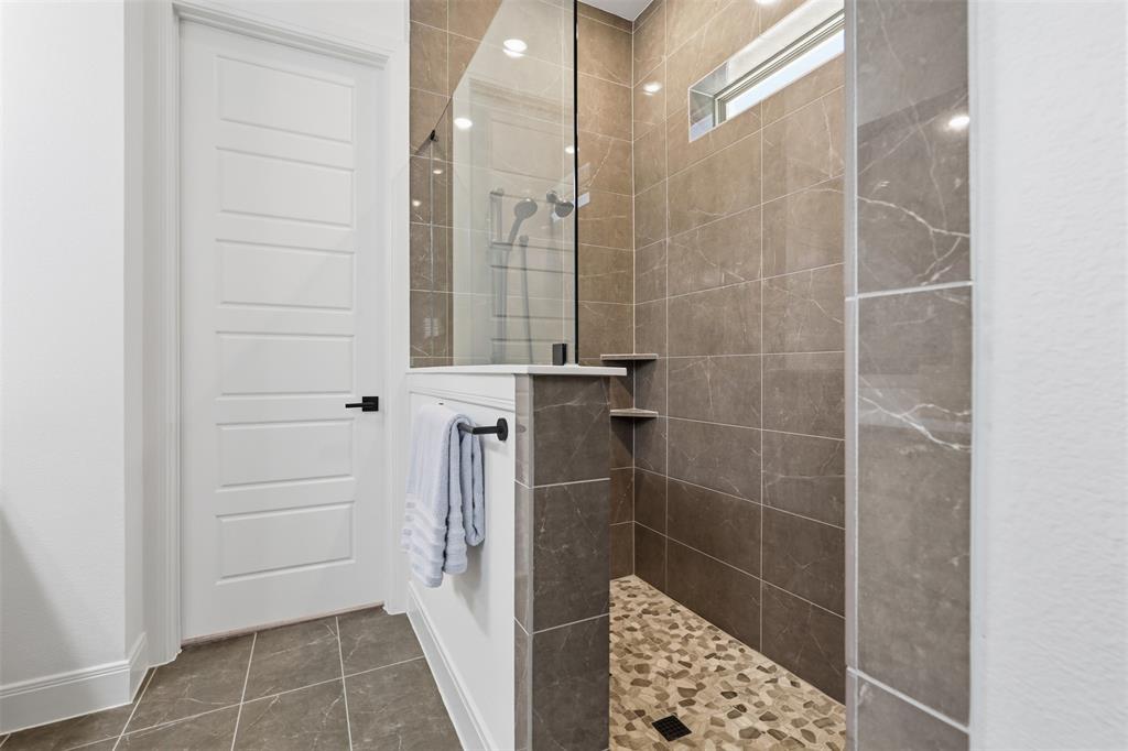 15413 Short Rdg Lane Fort Worth, TX 76008 - Photo 36 of 39 Walk-in shower featuring glass enclosure, stone tile walls, pebble flooring, and integrated shelving