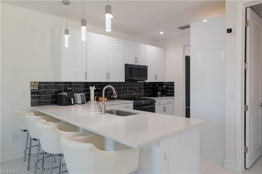 7510 Rockefeller Drive Naples, FL 34119 - Photo 21 of 31 Kitchen featuring white cabinets, a peninsula, decorative backsplash, black appliances, and hanging light fixtures