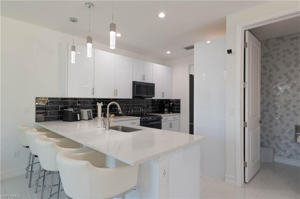 7510 Rockefeller Drive Naples, FL 34119 - Photo 5 of 31 Kitchen featuring a peninsula, backsplash, white cabinets, decorative light fixtures, and black appliances
