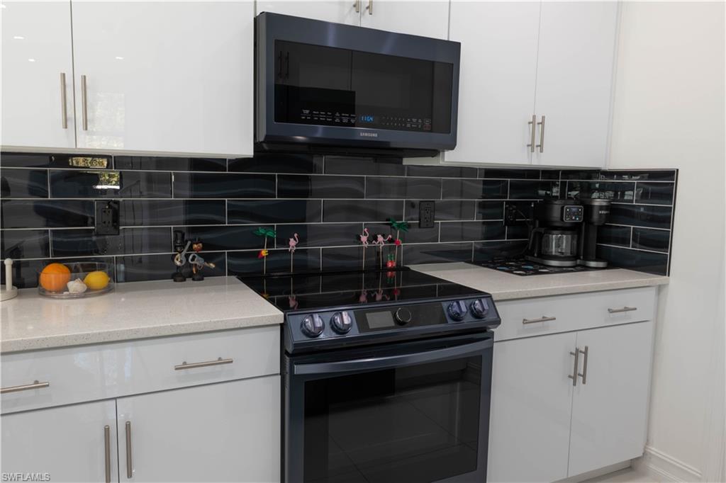 7510 Rockefeller Drive Naples, FL 34119 - Photo 7 of 31 Kitchen featuring black range with electric cooktop, white cabinetry, light stone counters, and decorative backsplash