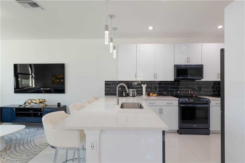7510 Rockefeller Drive Naples, FL 34119 - Photo 8 of 31 Kitchen with a peninsula, a kitchen breakfast bar, white cabinetry, black / electric stove, and decorative light fixtures