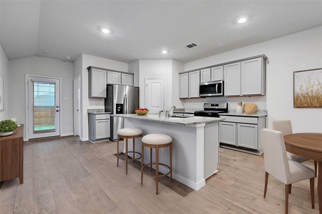 295 Evergreen Sumac Loop Kyle, TX 78640 - Photo 5 of 30 Kitchen featuring a breakfast bar area, stainless steel appliances, a center island with sink, light stone countertops, and gray cabinetry