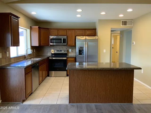 a kitchen with stainless steel appliances kitchen island granite countertop a stove a sink and a refrigerator