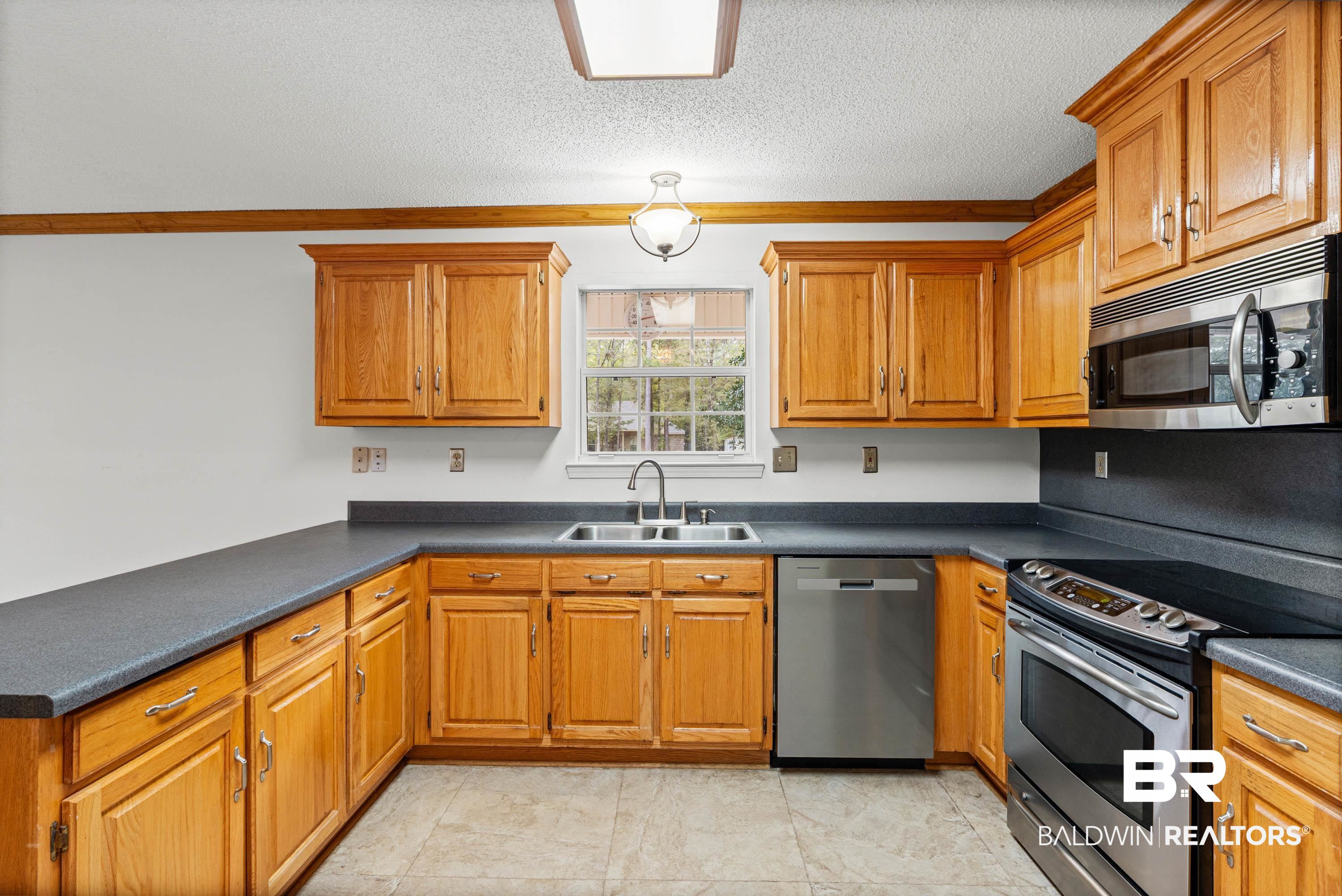 10140 Lakeview Road Bay Minette, AL 36507 - Photo 12 of 35 Kitchen with stainless steel appliances, dark countertops, wood finish cabinetry, a textured ceiling, and ornamental molding