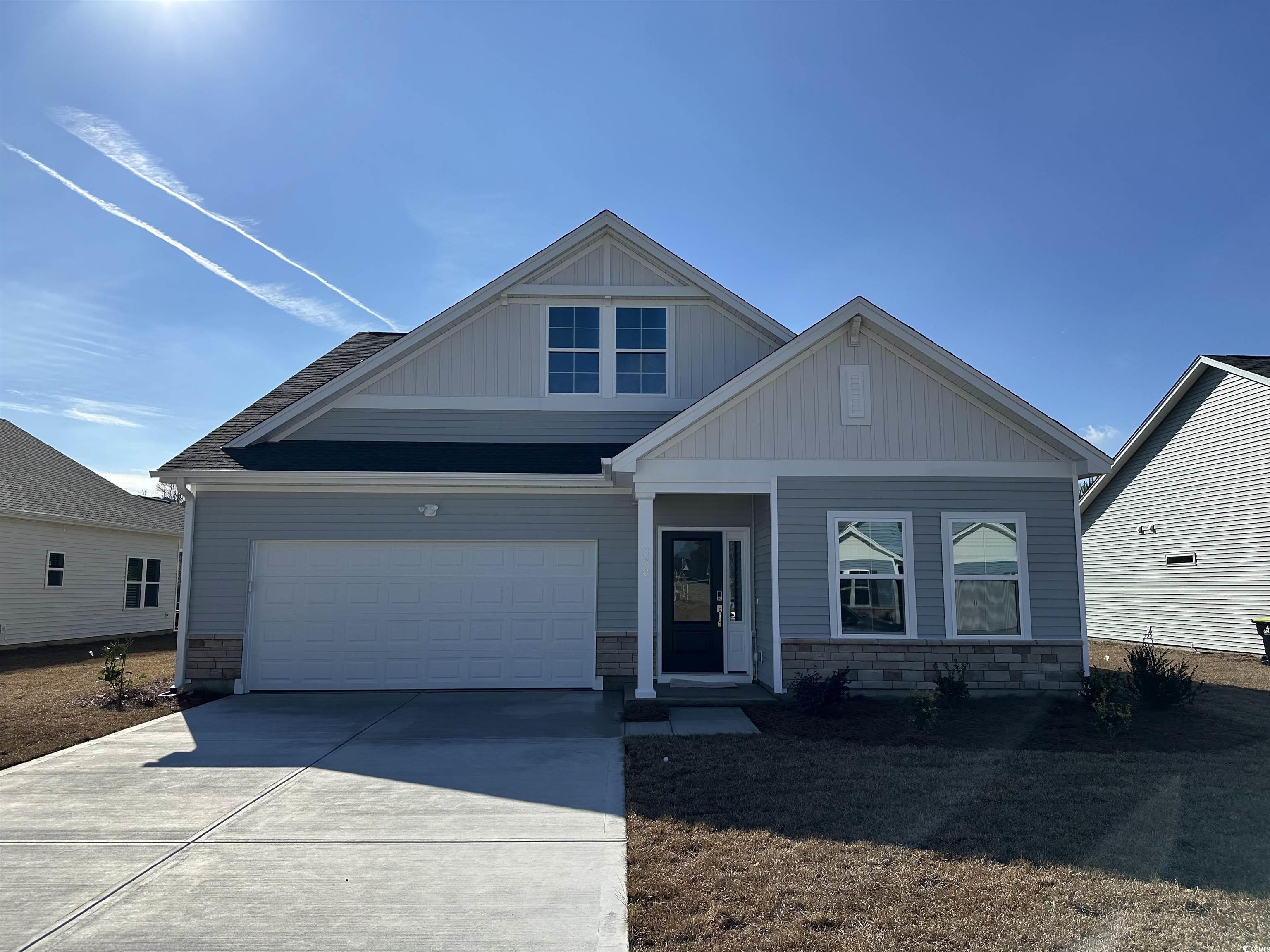 View of front of home with stone siding, a garage, concrete driveway, and board and batten siding