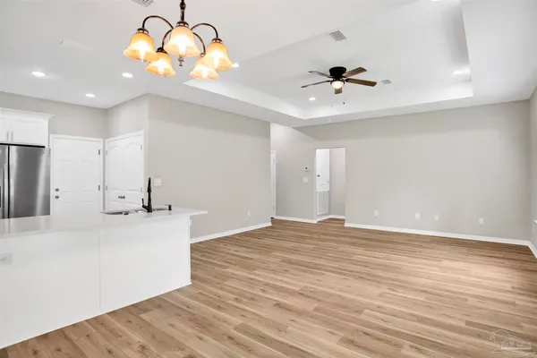 an empty room with chandelier fan and wooden floor