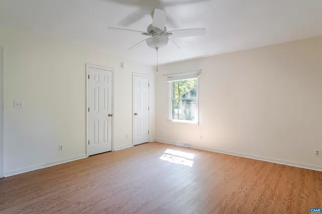an empty room with wooden floor chandelier fan and windows