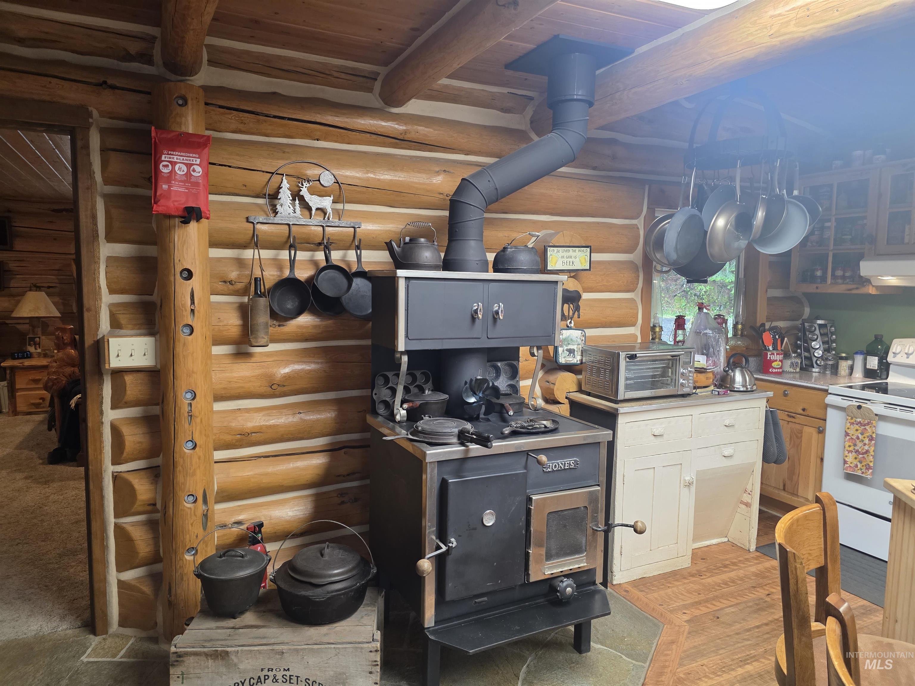 112 Three Forks Road Kamiah, ID 83536 - Photo 15 of 45 Log cabin interior featuring exposed log walls, wood-finish flooring, and a black wood-burning stove with an attached stovepipe