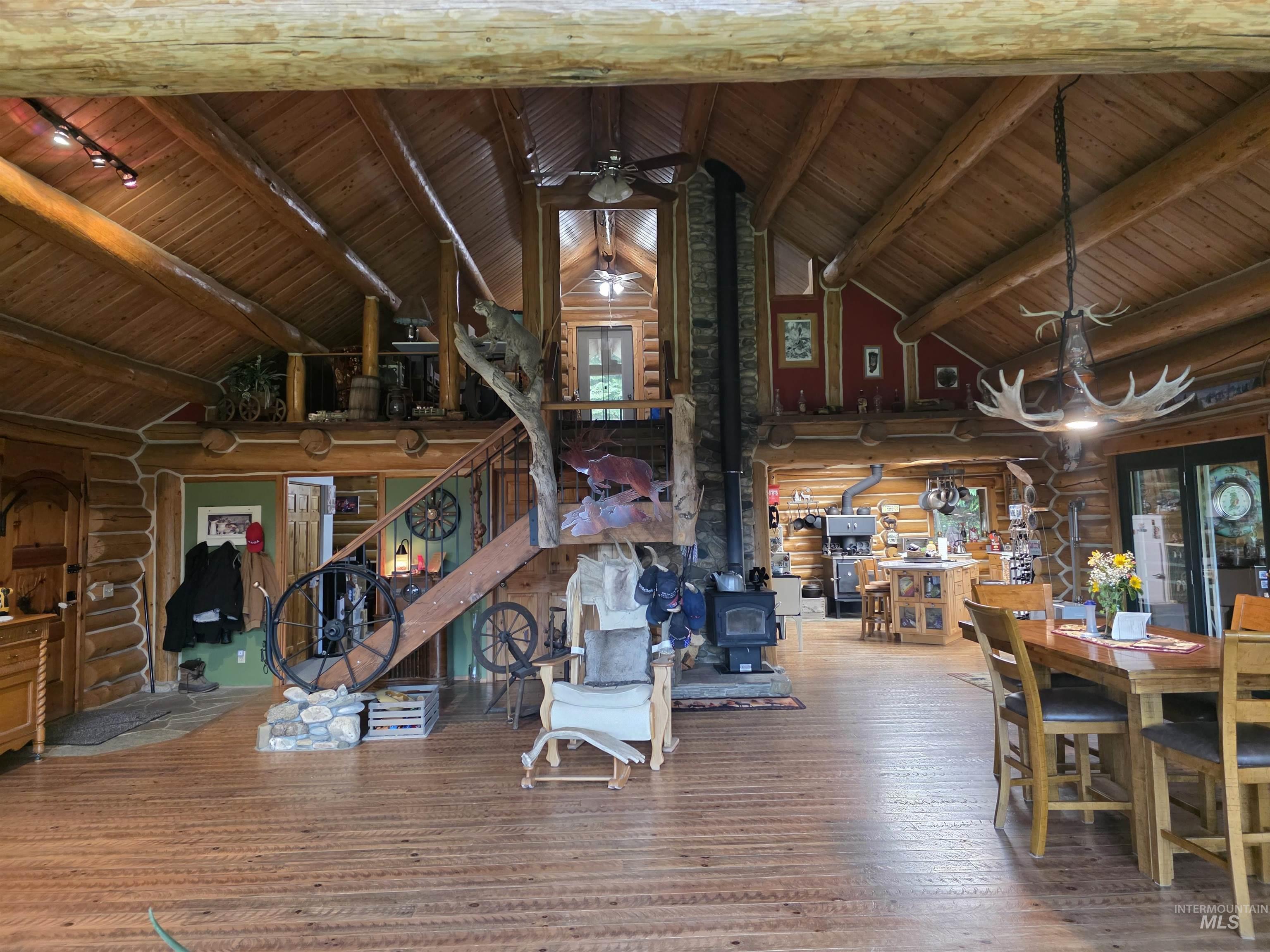 112 Three Forks Road Kamiah, ID 83536 - Photo 10 of 45 Spacious open-concept interior featuring natural log walls and ceiling beams, high vaulted ceilings, wood-finish flooring, a prominent stone-clad fireplace with a wood-burning stove, and a unique staircase with log newel posts
