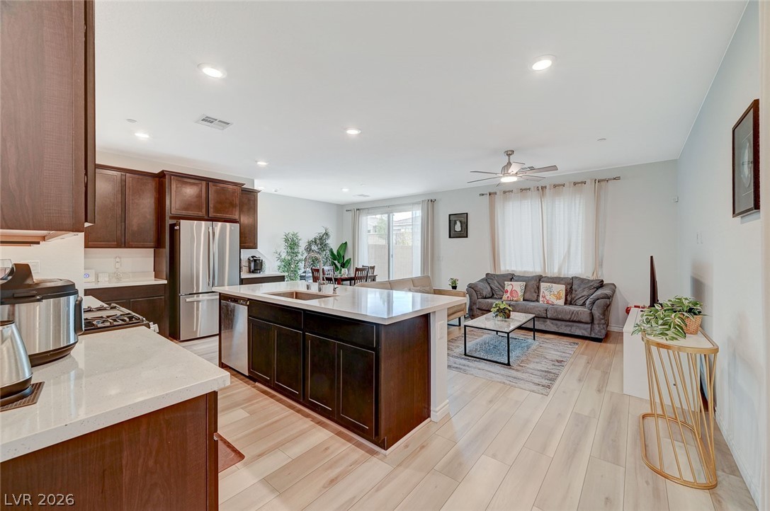 8855 Roadrunner Ravine Street Las Vegas, NV 89166 - Photo 15 of 54 Kitchen featuring stainless steel appliances, a sink, dark brown cabinets, light countertops, and a center island with sink