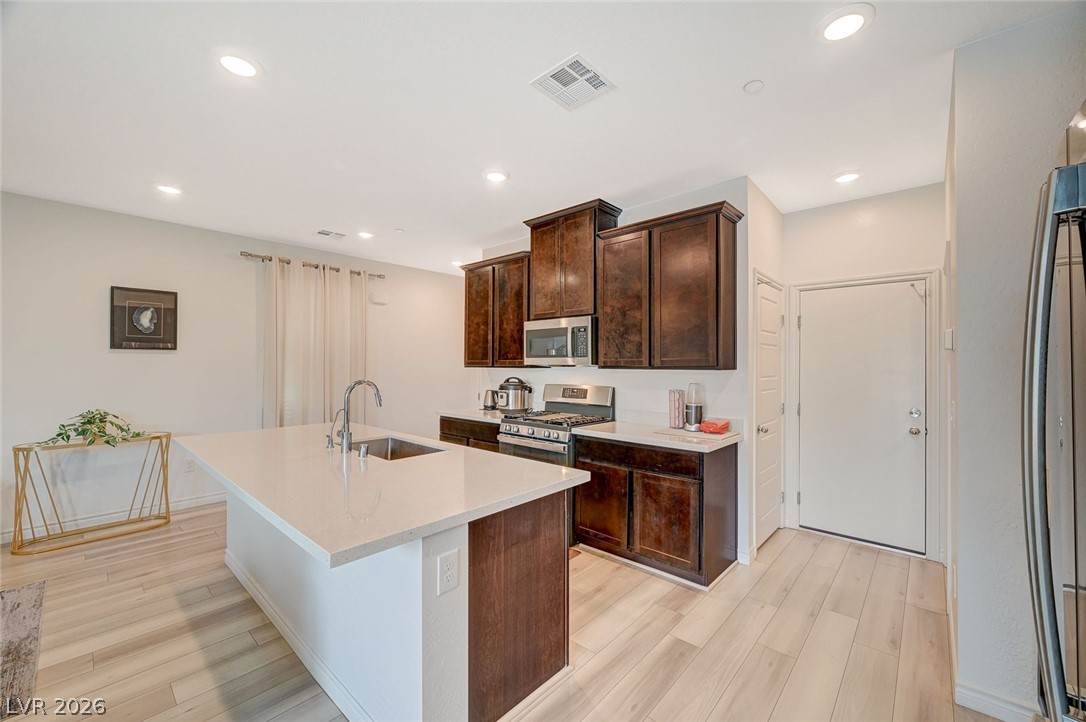 8855 Roadrunner Ravine Street Las Vegas, NV 89166 - Photo 18 of 54 Kitchen with visible vents, light wood-style flooring, appliances with stainless steel finishes, a kitchen island with sink, and a sink