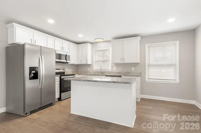 a kitchen with stainless steel appliances granite countertop a refrigerator a sink dishwasher a stove and white countertops with wooden floor