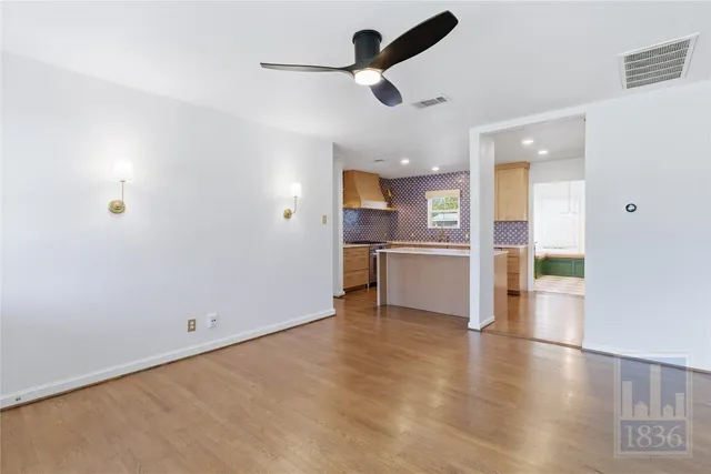 an empty room with wooden floor kitchen view and a window