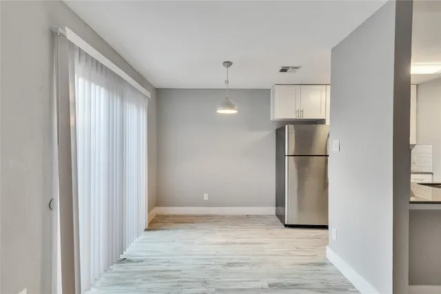 a view of empty room with wooden floor and kitchen