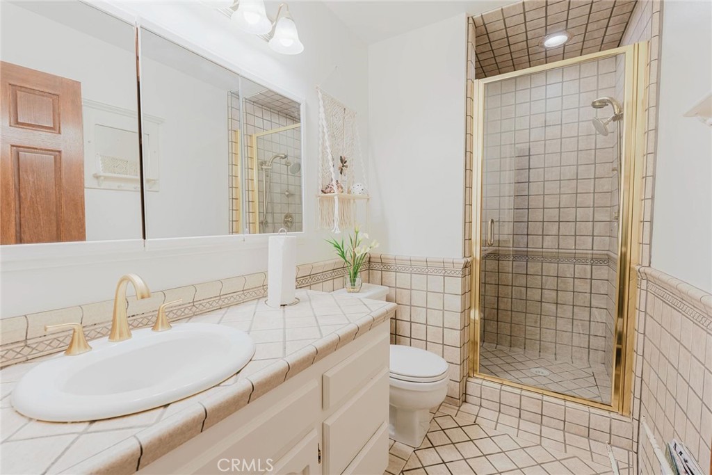25261 Avenida Rondel Valencia, CA 91355 - Photo 19 of 68 a bathroom with a granite countertop toilet a sink a mirror and shower