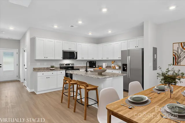 a kitchen with stainless steel appliances granite countertop a refrigerator a stove a sink and a dining table with wooden floor