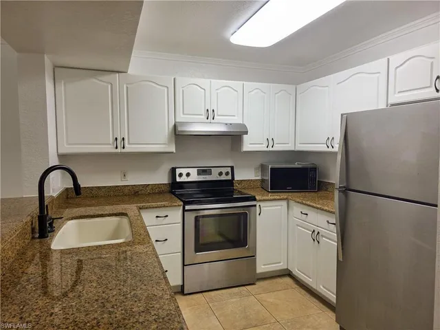 a white kitchen with stainless steel appliances granite countertop a stove a sink and a refrigerator