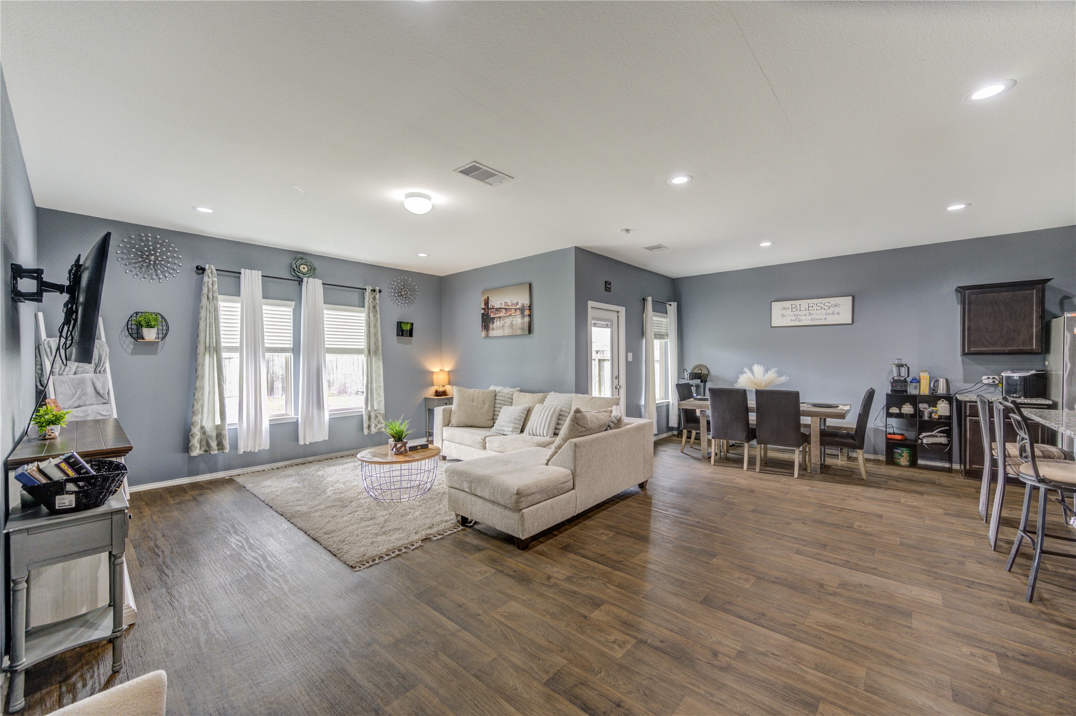 2306 Rainier Mist Road Spring, TX 77373 - Photo 6 of 28 Modern open-concept living area with neutral tones and abundant natural light. Features a comfortable sitting area, dining space, and a kitchen with bar seating, creating an inviting atmosphere for relaxation and entertaining.