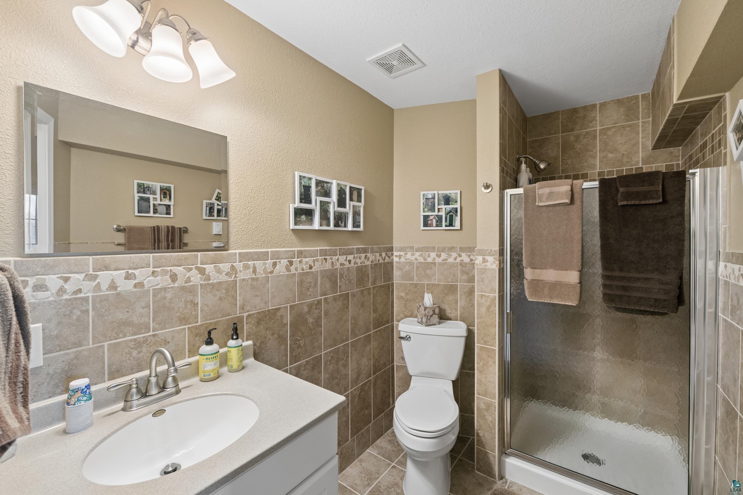 34590 Bay View Road, Unit 801 Bayfield, WI 54814 - Photo 25 of 36 Bathroom featuring a glass-enclosed shower, a vanity with an integrated sink, a large mirror, and tiled walls with a decorative border