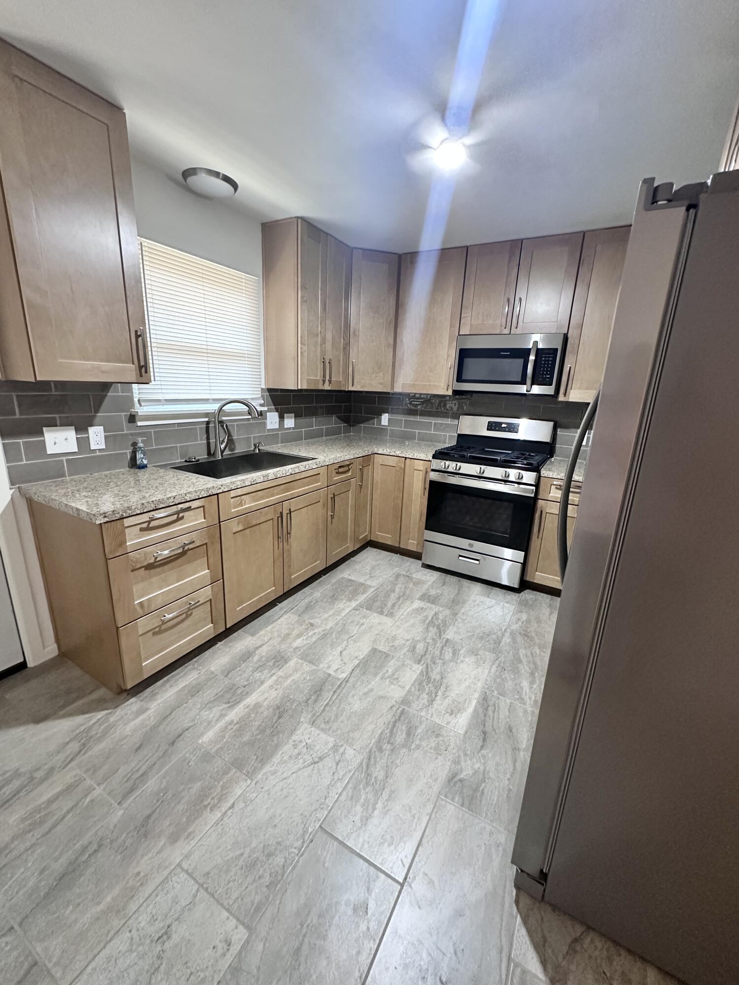 3719 30th Street, Unit A Lubbock, TX 79410 - Photo 3 of 16 a large kitchen with stainless steel appliances granite countertop a stove a sink dishwasher and a refrigerator with wooden floor