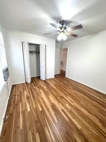 a view of an empty room with wooden floor and a ceiling fan