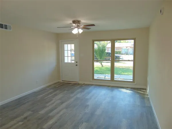 a view of an empty room with wooden floor and a window