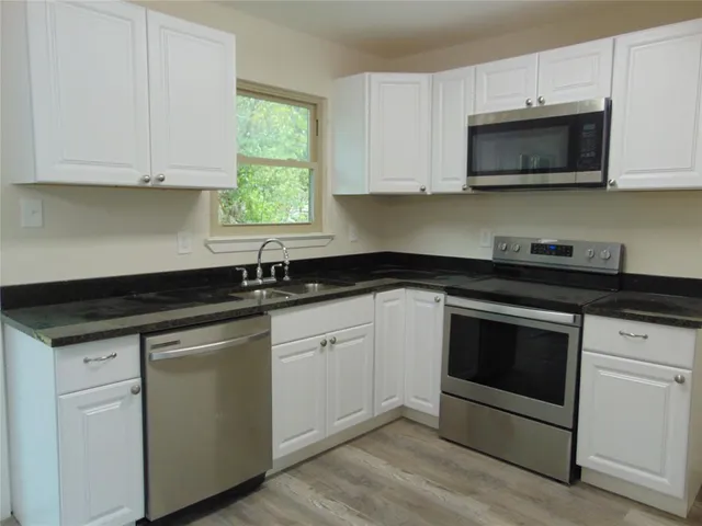 a kitchen with stainless steel appliances granite countertop white cabinets a sink and a microwave
