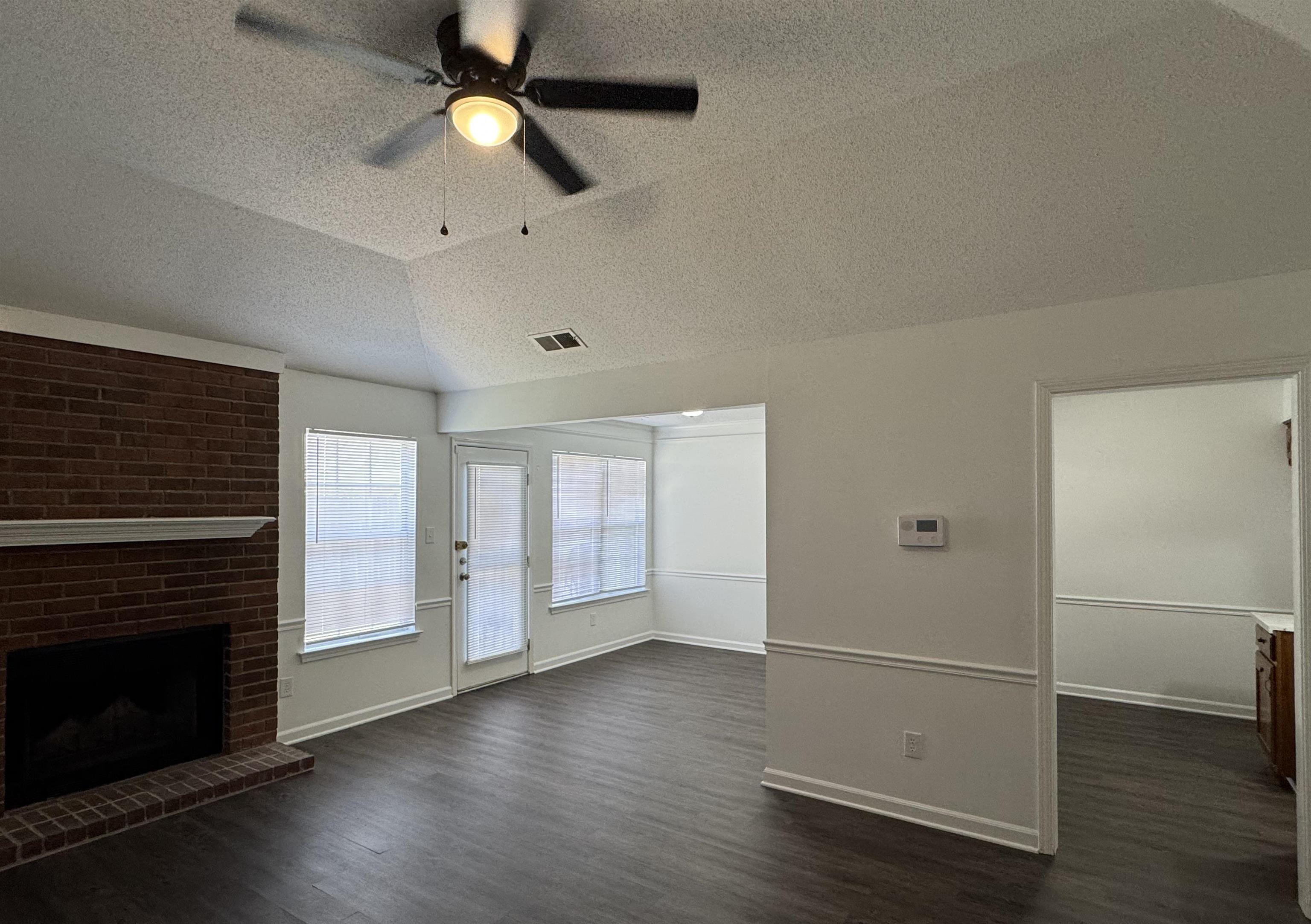 6932 Snyder Road Memphis, TN 38141 - Photo 4 of 15 an empty room with wooden floor a ceiling fan a fireplace and windows