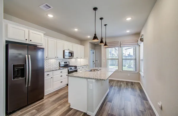 a kitchen with granite countertop a refrigerator a sink dishwasher a stove and white cabinets with wooden floor