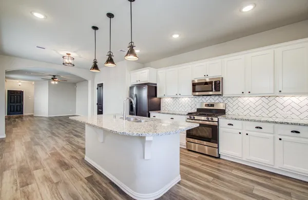 a large kitchen with stainless steel appliances granite countertop a stove a sink dishwasher a refrigerator white cabinets wooden floor and a fireplace