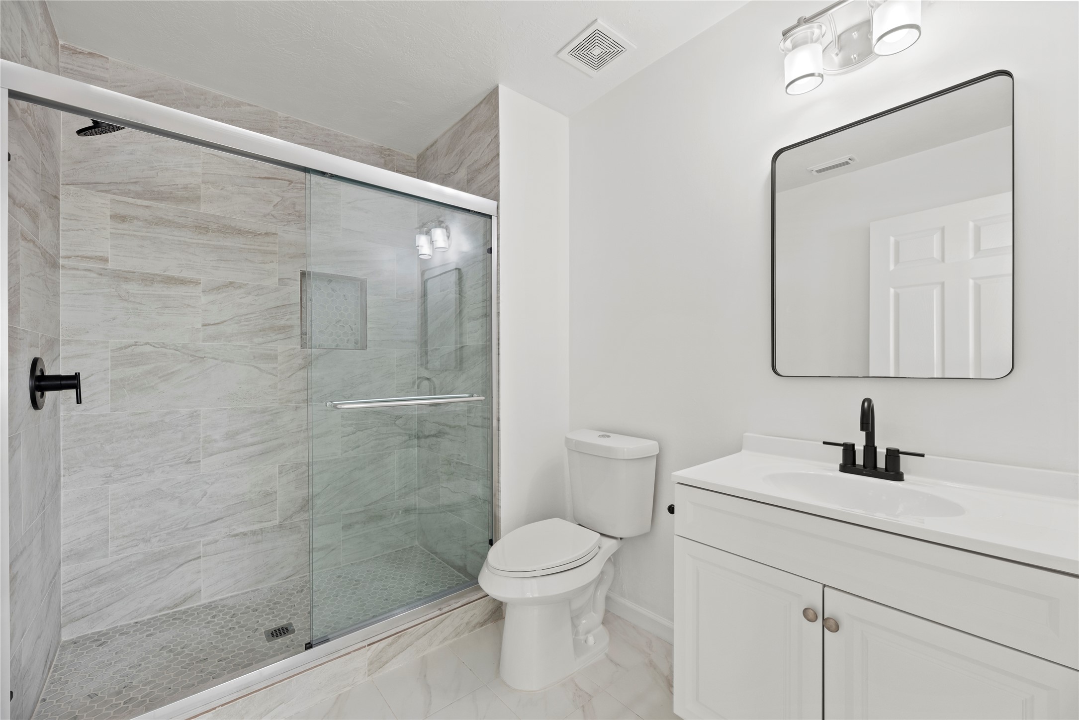 19910 Rustic Lake Lane Cypress, TX 77433 - Photo 13 of 21 This beautifully remodeled upstairs bathroom features a sleek quartz-topped vanity, modern black fixtures, and a stylish framed mirror with contemporary lighting. The spa-like walk-in shower showcases marble-look tile, a frameless glass enclosure, and a designer niche—perfectly blending style and function.