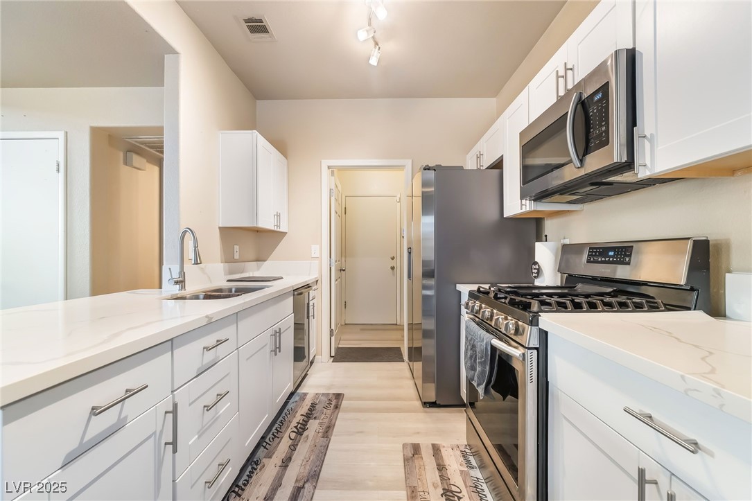 5322 Runningbrook Road Las Vegas, NV 89120 - Photo 10 of 25 Kitchen with stainless steel appliances, white cabinetry, light wood-type flooring, and light stone counters