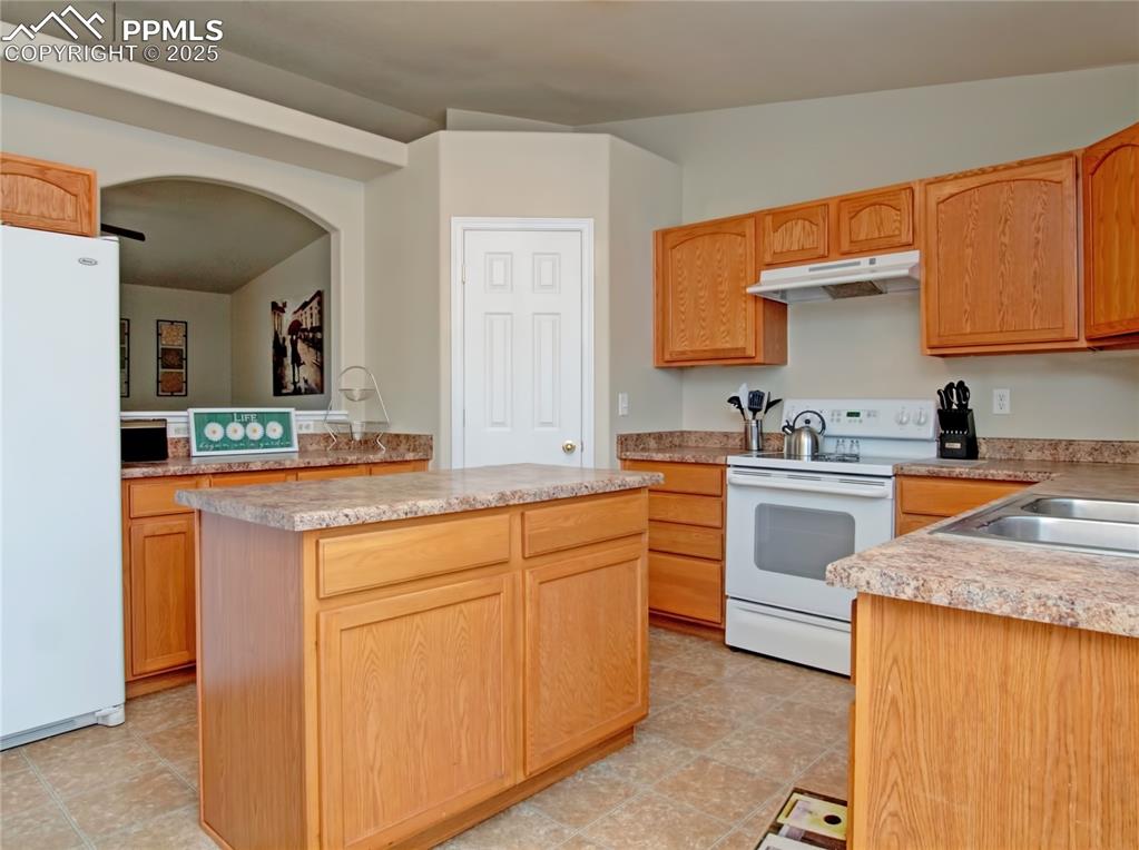 4806 Rusty Nail Point, Unit 202 Colorado Springs, CO 80916 - Photo 8 of 24 Kitchen with white appliances, a kitchen island, light countertops, under cabinet range hood, and arched walkways
