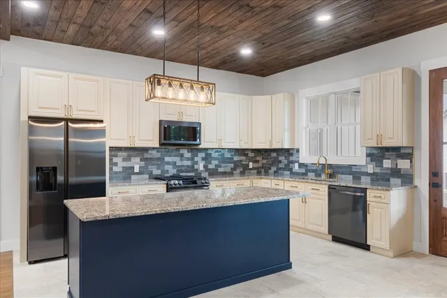 a kitchen with stainless steel appliances granite countertop a sink a stove a refrigerator cabinets and a window