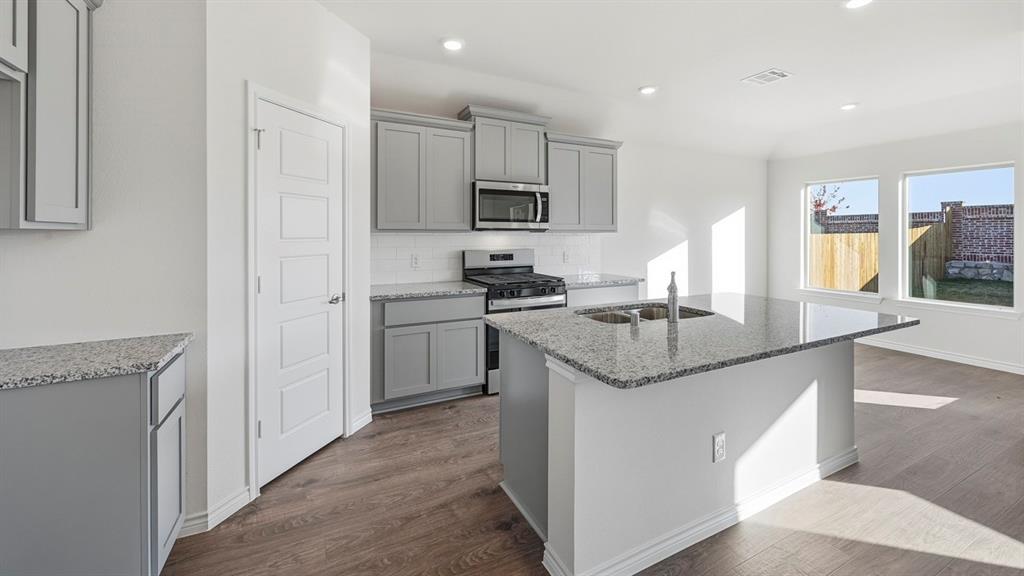 419 Epiphany Lane Lavon, TX 75166 - Photo 5 of 31 Kitchen featuring a central island with a double basin sink, gray cabinetry, stainless steel appliances, and wood-finish flooring