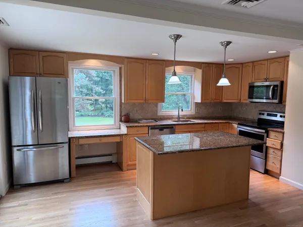 a kitchen with stainless steel appliances granite countertop a refrigerator a sink a stove and a wooden floors